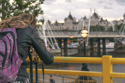 Rear view of woman by railing against bridge in city