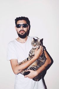 Portrait of young man holding cat while standing against wall