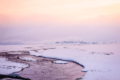 Aerial view of frozen water on land against sky during sunset