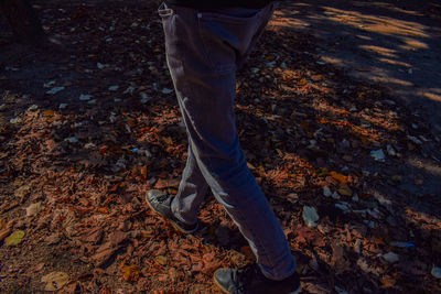 Low section of man walking on fallen autumn leaves