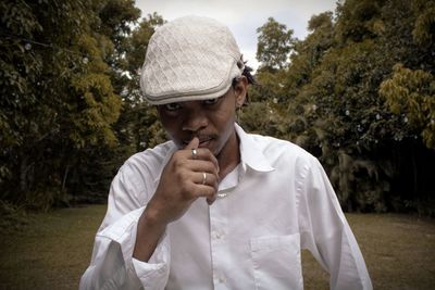 Portrait of man holding hat against trees