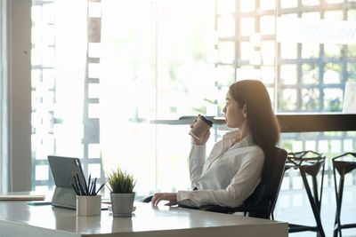 Young woman using smart phone while sitting on table
