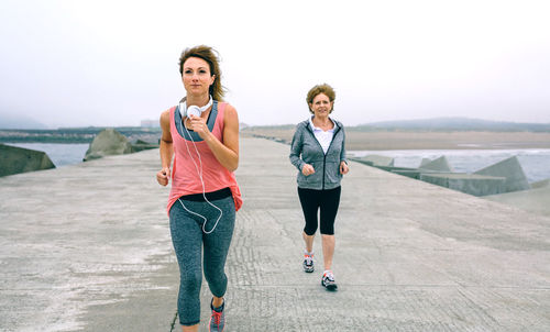 Woman with mother jogging on pier against sky