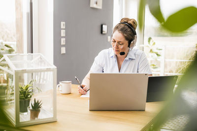 Female entrepreneur wearing wireless headphones while working on document at desk