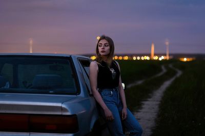 Thoughtful young woman standing by car on land at dusk