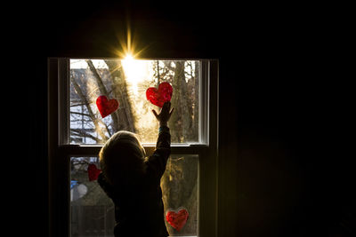 Rear view of boy sticking heart shapes on window at home