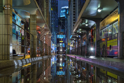 Cable car amidst buildings on wet street in city at night