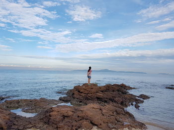 Full length of woman standing on rock by sea against sky