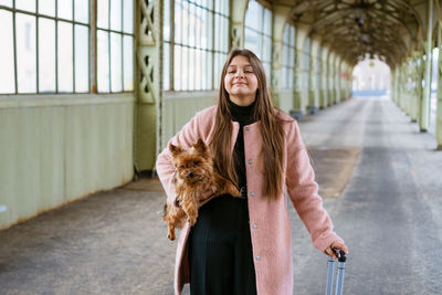 Woman traveler tourist walks with luggage and dog at train station in pink