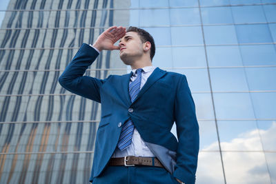 Low angle view of businessman shielding eyes against skyscraper