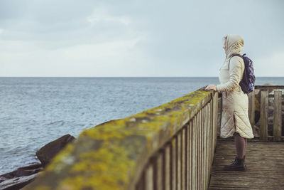 Rear view of woman standing on pier over sea against sky