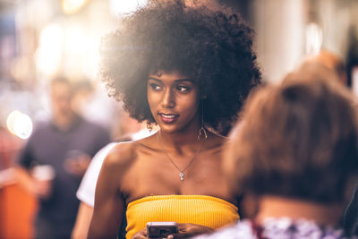 Thoughtful young woman looking away while holding smart phone on city street