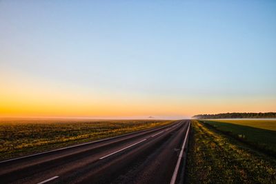 Road amidst field against sky during sunset