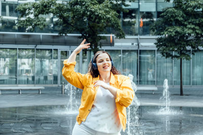 Confident plus size curvy happy young woman dancing street fountains modern background.