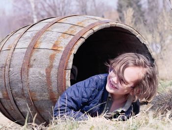 Smiling boy looking away while lying in barrel over grass