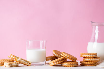 Sandwich cookies and a glass of milk on a pink background.