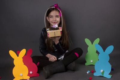 Portrait of smiling girl with eater bunny and pom pom in basket against gray background