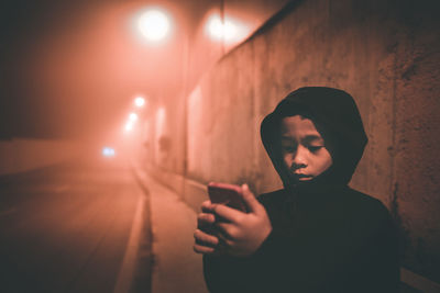 Boy using phone while standing on sidewalk at night