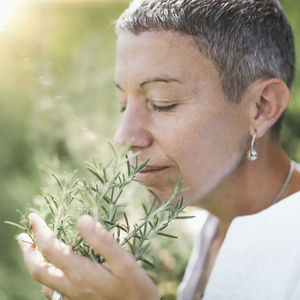 Woman with eyes closed holding while smelling rosemary plant