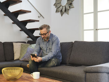 Man using phone alone on sofa in living room at home