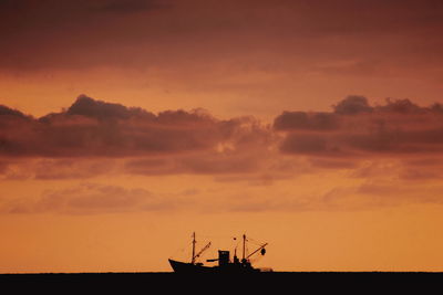 Silhouette boat in sea against cloudy sky during sunset