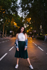 Portrait of young woman standing on road against trees