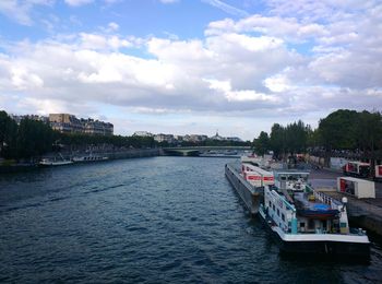 Boats in river against cloudy sky