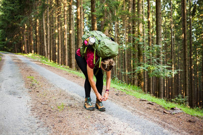 Full length of woman tying shoe lace on road in forest