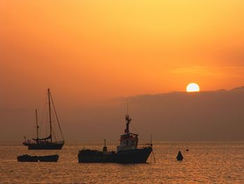 Silhouette sailboats on sea against orange sky during sunset