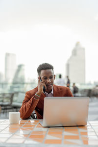 Businessman talking on phone while using laptop in cafe