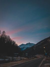 Road by trees against sky during sunset