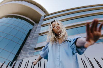 Young blond woman gesturing while standing in front of building