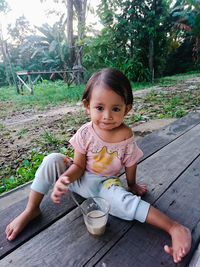 Portrait of girl eating food while sitting on wooden floor in yard