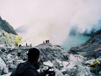Rear view of man looking at tourists by ijen crater