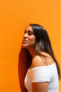 Young woman with closed eyes leaning on orange wall