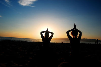 Silhouette people on beach against sky during sunset