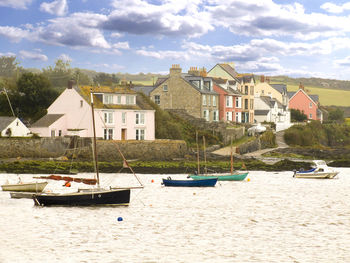 Sailboats moored on river by houses against sky