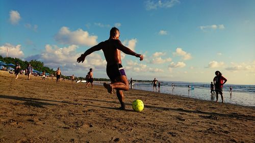 People playing soccer ball on beach against sky