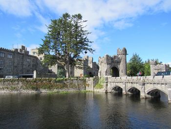 Arch bridge over river by buildings against sky