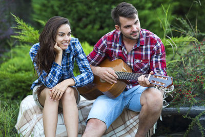 Woman sitting with boyfriend playing guitar while sitting against plants