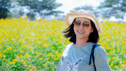 Portrait of smiling woman standing by yellow flowering plants