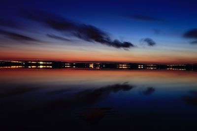 Illuminated city by sea against sky at sunset