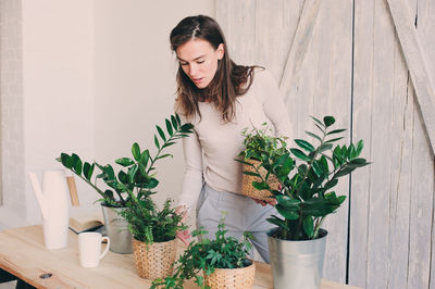 Young woman standing by potted plant on table at home