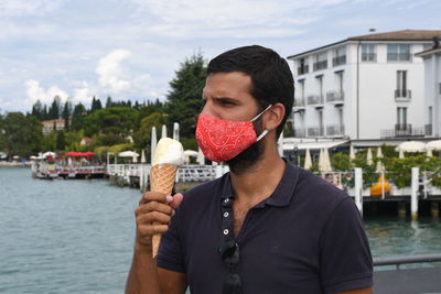 Portrait of man holding ice cream in city against sky