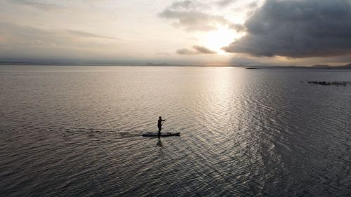 Silhouette person in sea against sky during sunset