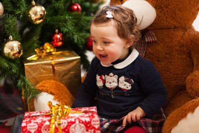 Cute girl with stuffed toy and gifts against christmas tree at home