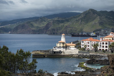 Buildings at waterfront against cloudy sky