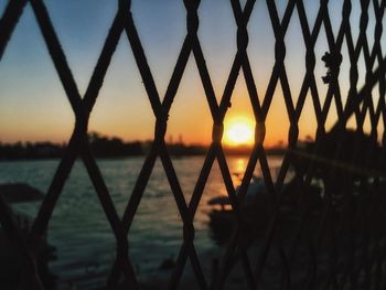 Silhouette fence by lake against sky during sunset