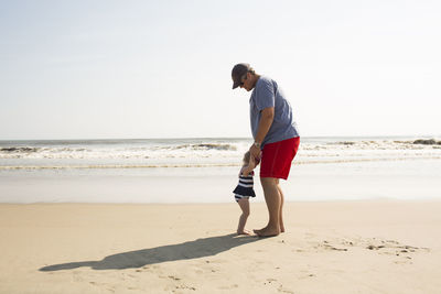 Father and daughter enjoying at beach against sky during sunny day