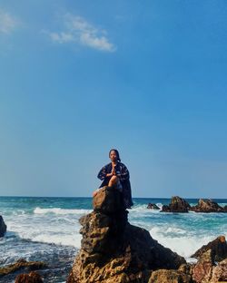 Man sitting on rock by sea against sky